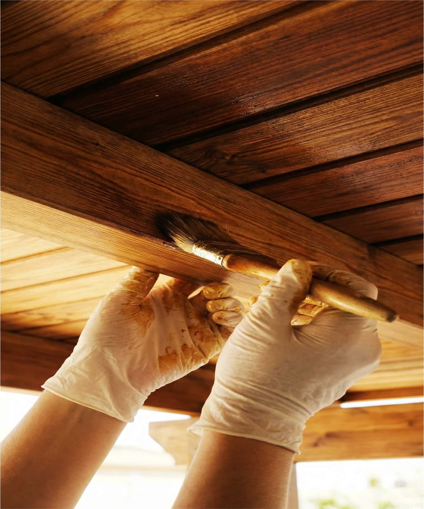 Operario limpiando las vigas de una pérgola de madera con chorro a presión y equipo de protección.