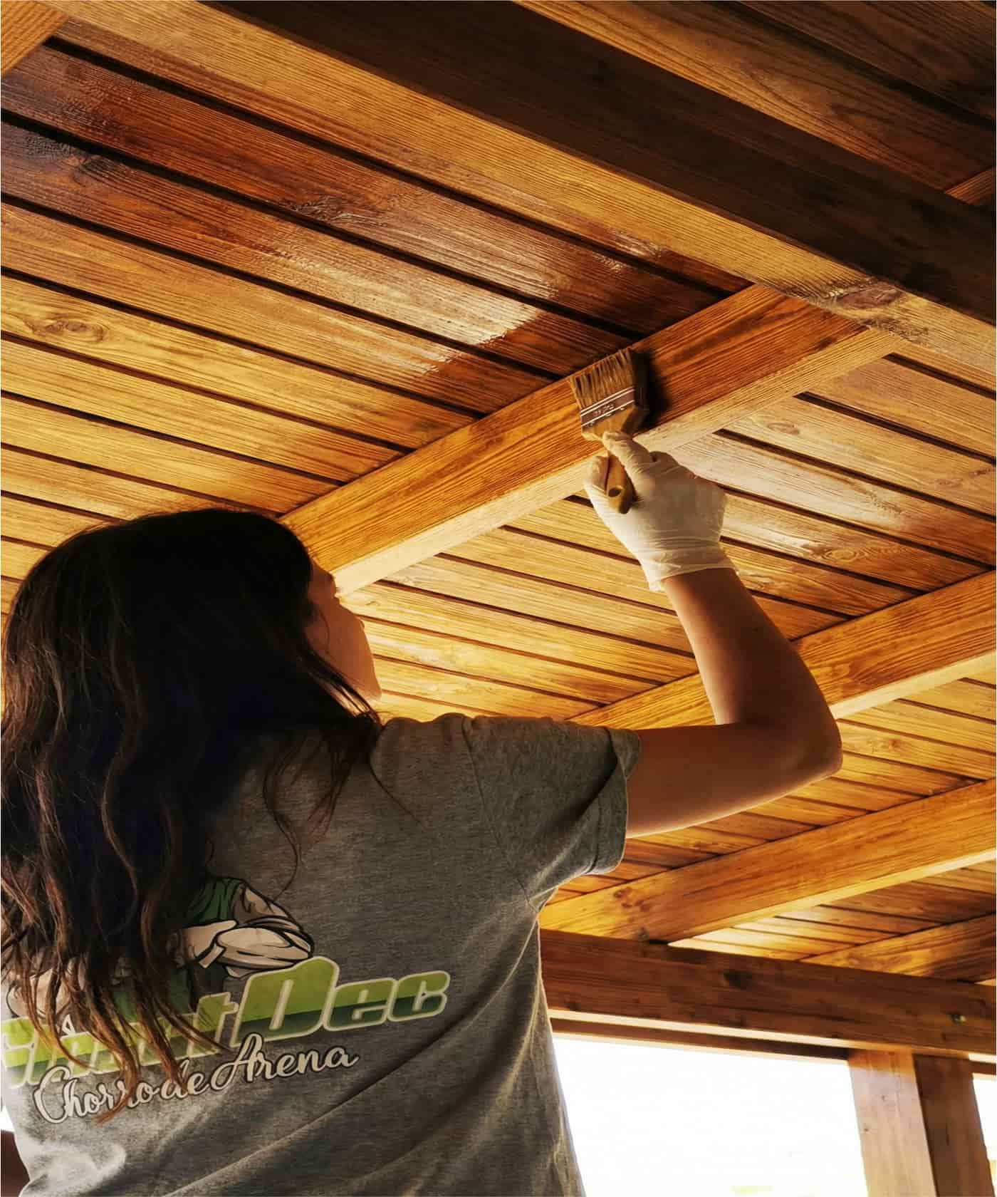 Persona aplicando tratamiento protector con brocha en el techo de una pérgola de madera.