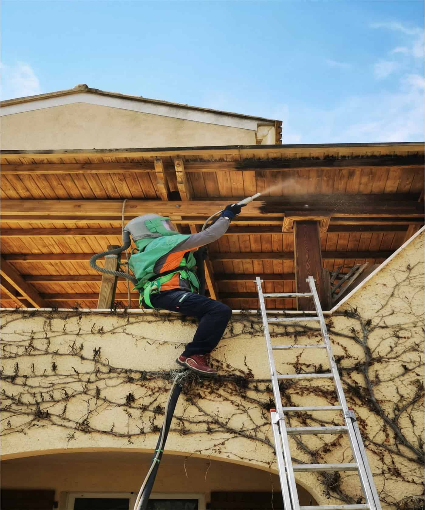 Operario con equipo de protección limpiando con chorro a presión el alero de una cubierta de madera.